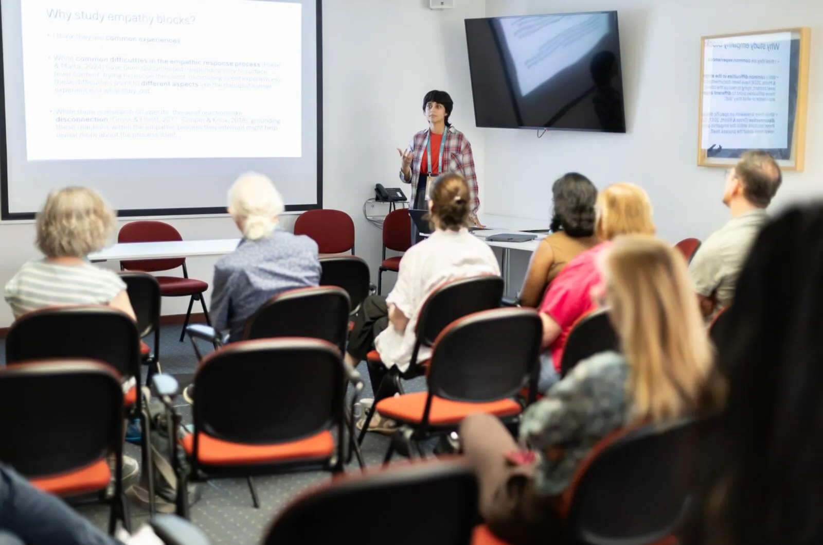 A presenter speaking to a seated audience in a small conference room