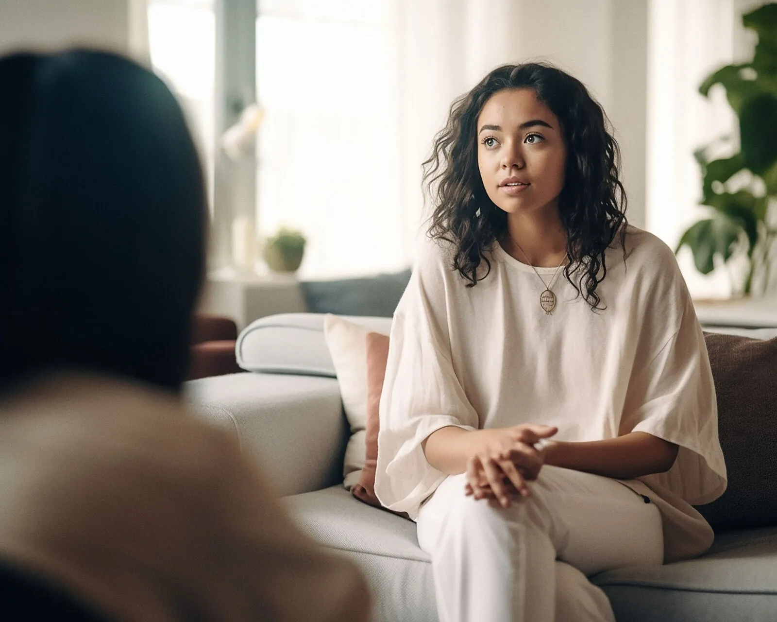 A woman sitting on a sofa in a therapy session, looking thoughtfully towards her therapist